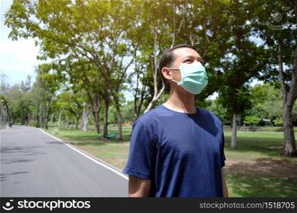 Asian young man in sportwear and wearing mask protection for covid-19 virus and exercise for running and jogging in the garden. Social distancing and new normal life Concept