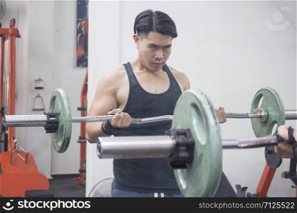 Asian young man lifting barbell in front of the mirror