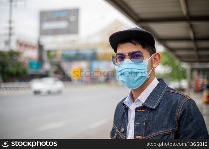 Asian Young man standing in the city and wearing protection mask on face for protection air pollution, particulates and for protection flu virus, influenza, coronavirus at city