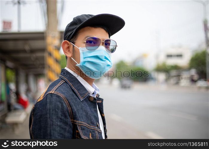 Asian Young man standing in the city and wearing protection mask on face for protection air pollution, particulates and for protection flu virus, influenza, coronavirus at city