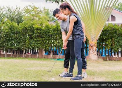 Asian young man support teaching training woman to play perfect golf while standing together in nature a field garden park. Couple trainer giving a lesson on the golf course