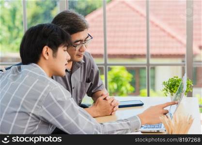 Asian young man teaching senior father how to use a modern laptop computer together in the living room at home, Son helping Dad to use the laptop for web application online