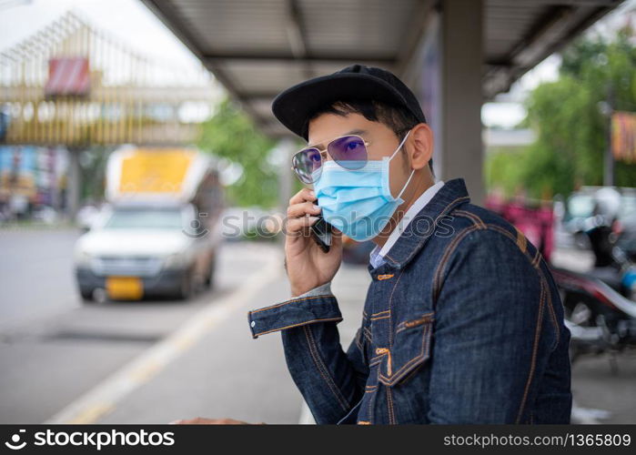 Asian Young man using smart phone in the city and wearing face mask for protection air pollution, particulates and for protection flu virus, influenza, coronavirus