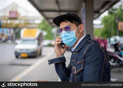 Asian Young man using smart phone in the city and wearing face mask for protection air pollution, particulates and for protection flu virus, influenza, coronavirus