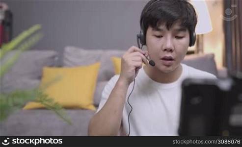 Asian young man wear headset having conversation with clients, microphone voice call interaction with client, Online customer care live chat with staff, work from home, relax casual at home clothing