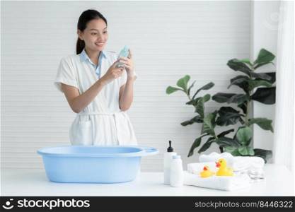 Asian young mother wear bathrobe is reading ingredients label of liquid soap or sh&oo carefully for product does not cause allergic reactions for her baby while prepare bathing newborn at home