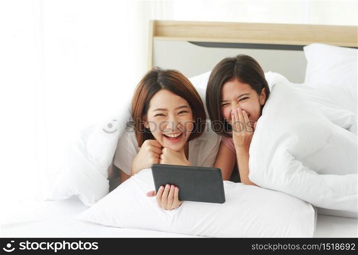 Asian young sisters lovely couple on white bed and smiling together for online Social with laptop in bedroom. Homosexual women or Lesbian in love. LGBT Asian and Holiday concept.