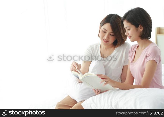 Asian young sisters lovely couple on white bed hand holding a book and reading notebook together in bedroom. Education and students Concept