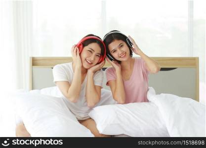 Asian young sisters lovely couple on white listen to music with Headphones and dancing together in bedroom. Homosexual women or Lesbian in love. LGBT Asian and Holiday concept.
