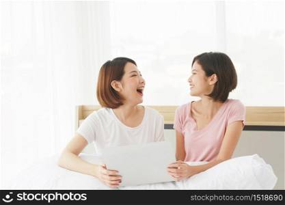 Asian young sisters lovely couple sitting on white bed and smiling together for online Social with laptop in bedroom. Homosexual women or Lesbian in love. LGBT Asian and Holiday concept.