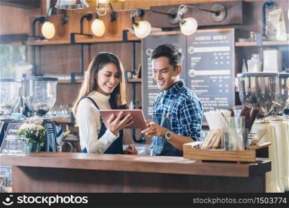 Asian Young Small business owner talking with colleagues and using technology tablet in front of counter bar, entrepreneur and startup, preparing for service to customer in cafe store concept