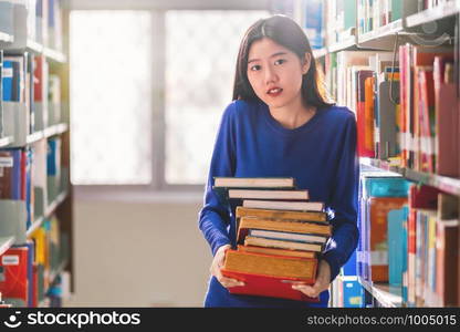 Asian young Student in casual suit holding after searching the book from book shelf in library of university or colleage with various book background, Back to school concept