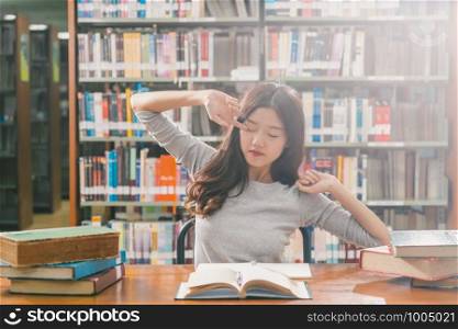Asian young Student in casual suit reading and doing stretch oneself in library of university or colleage with various book and stationary on the wooden table over the book shelf, Back to school