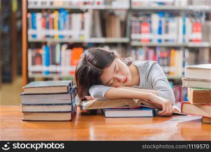 Asian young Student in casual suit reading and sleeping on the wooden table with various book in library of university or colleage over the book shelf, Back to school concept