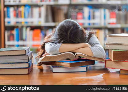 Asian young Student in casual suit reading and sleeping on the wooden table with various book in library of university or colleage over the book shelf, Back to school concept