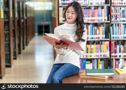 Asian young Student in casual suit reading the book in library of university or colleage on the wooden table over the book shelf background, Back to school concept
