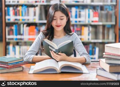Asian young Student in casual suit reading the book on the wooden table in library of university or colleage with various book and stationary over the book shelf background, Back to school concept