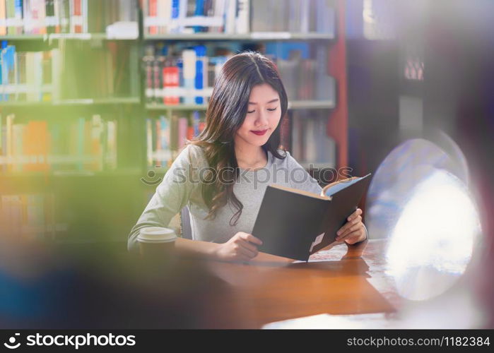 Asian young Student in casual suit reading the book with a cup of coffee in library of university or colleage on the wooden table over the book shelf background, Back to school concept