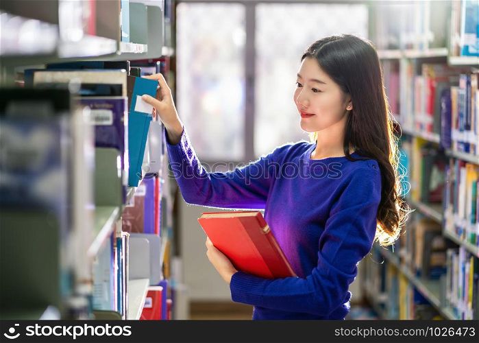 Asian young Student in casual suit searching the book from book shelf in library of university or colleage with various book background, Back to school concept