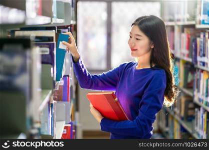 Asian young Student in casual suit searching the book from book shelf in library of university or colleage with various book background, Back to school concept