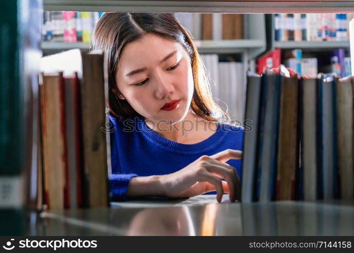 Asian young Student in casual suit searching the book in serious feeling from book shelf in library of university or colleage with various book background, Back to school concept