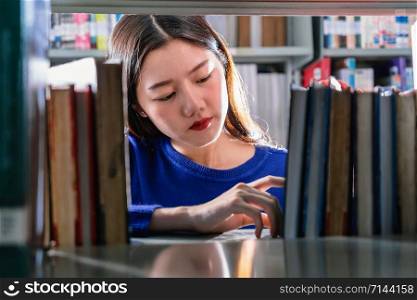 Asian young Student in casual suit searching the book in serious feeling from book shelf in library of university or colleage with various book background, Back to school concept