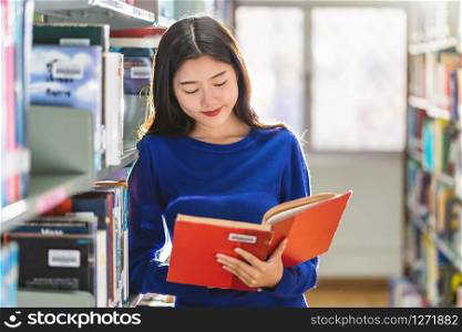 Asian young Student in casual suit standing and reading the book at book shelf in library of university or colleage with various book background, Back to school concept