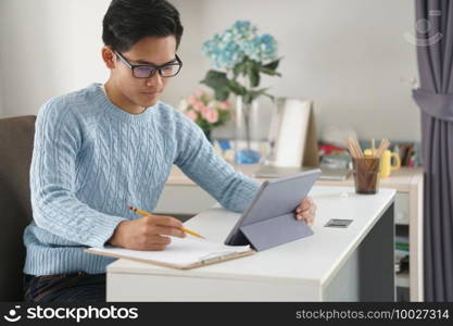 asian young teenage student man teenager entrepreneur working with tablet studying learning online at home. e-learning webinar meeting. social distance in covid pandemic