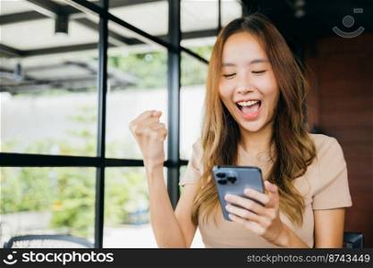 Asian young woman celebrating work success near windows in morning with mobile phone, Beautiful female successful excited she saised hands with smartphone winner gesture outside