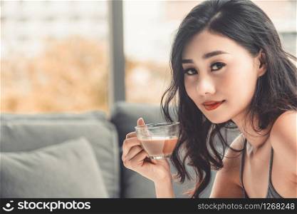 Asian young woman drinks coffee in the morning while sitting on sofa couch.
