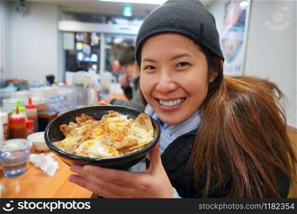 Asian young woman enjoy with japanese food which have rice with beef Barbecue, onsen egg and cheese in the bowl in fish market, tokyo, japan
