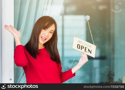 "Asian young woman glad and smiling she notice sign wood board label "WELCOME OPEN" hanging through glass door front shop, Business turning open after coronavirus pandemic disease, back to new normal"