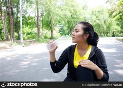 Asian young woman in black and yellow sportwear Thirsty and drinking water in bottle after exercise and running in the garden.