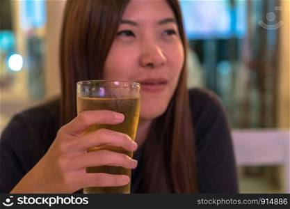 Asian young woman in happiness action and drinking beer in pub and restaurant with low light place, relax and drink concept