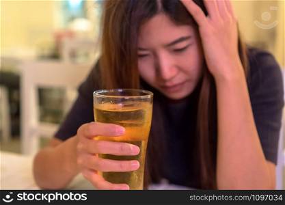Asian young woman in lonely and depressed action and holding glass of beer in pub and restaurant with low light place, depression and drinking concept