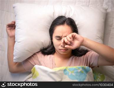 Asian young woman is sleepy while alarm clock on bed in the morning.