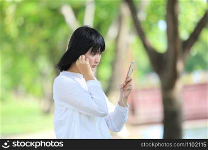 Asian young woman listening music on smart phone portrait with green tree background