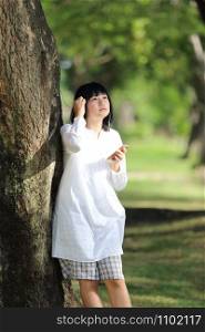 Asian young woman listening music on smart phone portrait with green tree background
