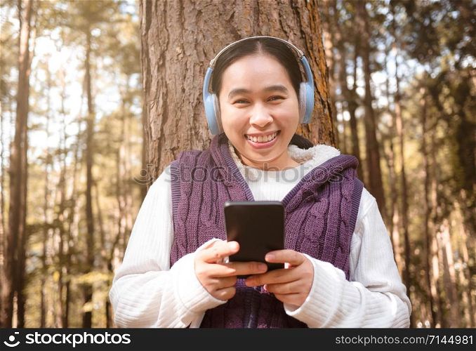 Asian young woman listening to music by headphone in the garden. Technology and relaxation concept.