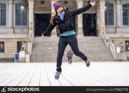 Asian Young woman playing the snow and jumping when Snow just fell, travel and excited concept, wool hat with scart and overcoat for winter season