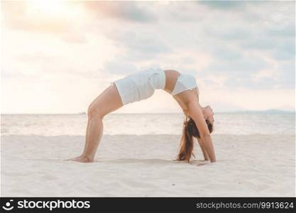 Asian young woman practice Yoga bridge Pose on the sand and beach with sunset beautiful sea in Tropical island,Feel comfortable and relax in holiday,Vacation Yoga Concept