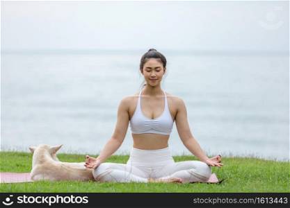 Asian young woman practice yoga lotus pose to meditation with dog on the beach feeling so happiness and cheerful,Travel in tropical beach in Thailand,vacations and relaxation Concept
