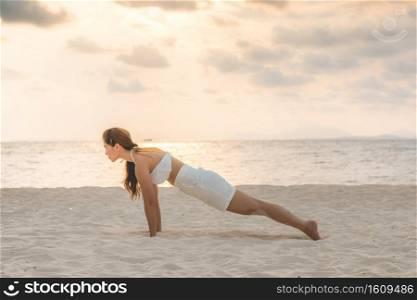 Asian young woman practice yoga Plank or Phalakasana Pose on the sand and beach with sunset beautiful sea in Tropical island,Feeling comfortable and relax in holiday,Vacations Yoga Concept