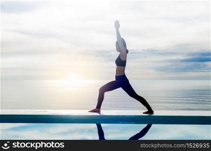 Asian young woman practice yoga Warrior I or Virabhadrasana Pose on the beach with beautiful sea,Feeling so comfortable and relax in holiday