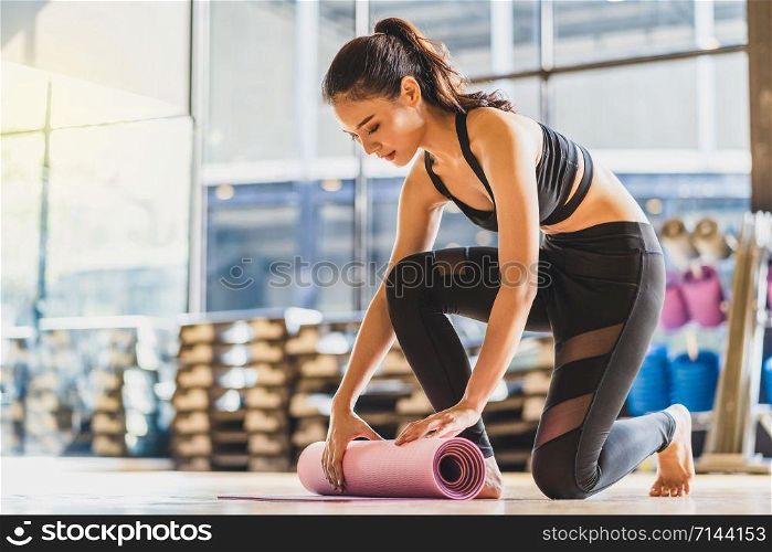 Asian Young woman rolling and unrolling yoga mat before and after practiced yoga sport, preparing for healthy or Meditation Exercise, wearing sportswear bra and pants, sports and healthcare concept