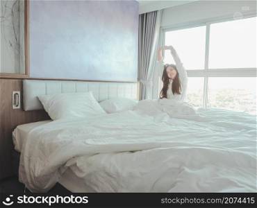 Asian young woman stretching morning wake up in bedroom on bed with white curtain background.