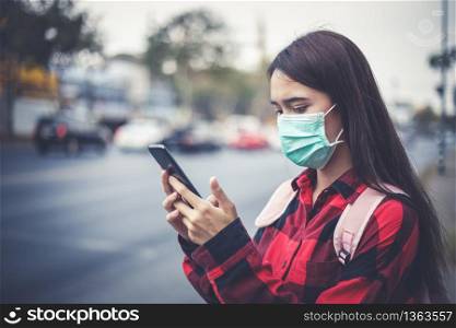 Asian Young woman using smart phone in the city wearing face mask because of air pollution, particulates and for protection flu virus, influenza, coronavirus