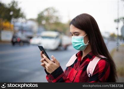 Asian Young woman using smart phone in the city wearing face mask because of air pollution, particulates and for protection flu virus, influenza, coronavirus