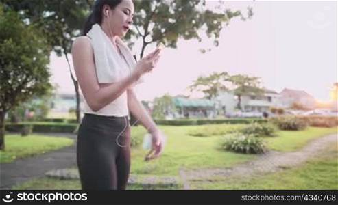 asian young woman using smartphone choosing music getting ready warm up before running at outdoors park during sunset hour, relaxing workout, , new normal modern life, quality time at the park