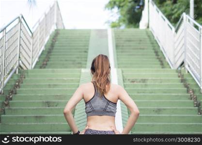 Asian young woman warm up body stretching before morning exercise and jogging under warm light morning. Healthy young asian woman exercising by running on step stair. Woman exercise outdoor concept.